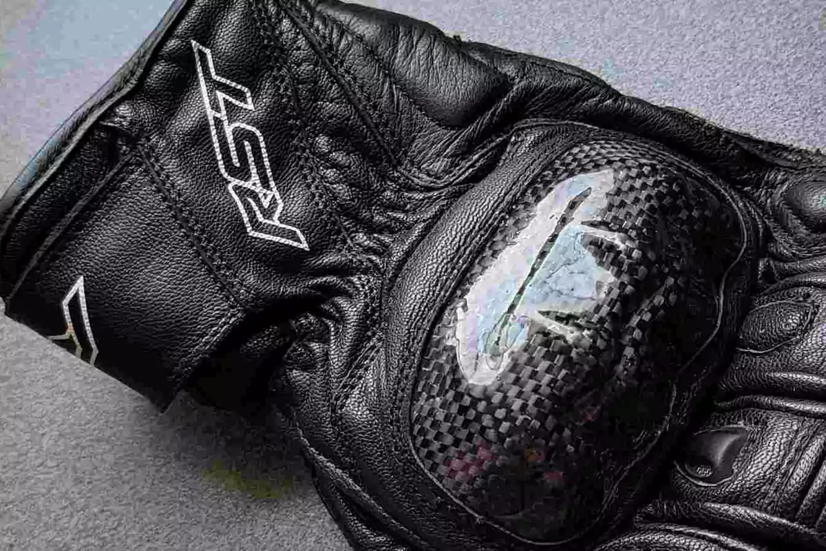 Guante de motociclista negro con protección de fibra de carbono y logotipo RST visible sobre una superficie gris Guante de motociclista negro con protección de fibra de carbono y logotipo RST visible sobre una superficie gris