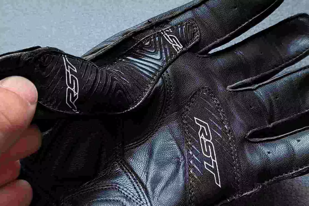 Guante negro de motociclista con logotipo RST sostenido por una mano Guante negro de motociclista con logotipo RST sostenido por una mano