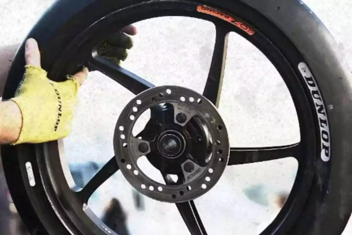 Person with yellow gloves holding a motorcycle wheel with a Dunlop tire Person with yellow gloves holding a motorcycle wheel with a Dunlop tire