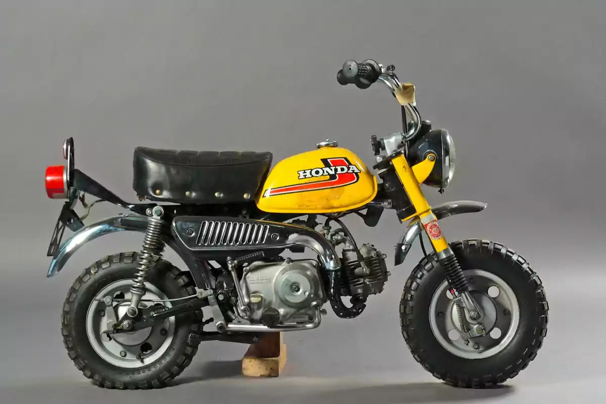 Motocicleta Honda pequeña de color amarillo con asiento negro y llantas gruesas sobre un fondo gris Motocicleta Honda pequeña de color amarillo con asiento negro y llantas gruesas sobre un fondo gris