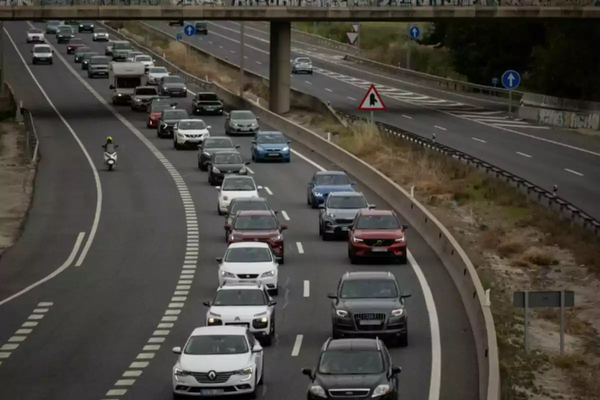 Tráfico denso en una autopista con varios coches y una motocicleta avanzando por el carril izquierdo Tráfico denso en una autopista con varios coches y una motocicleta avanzando por el carril izquierdo