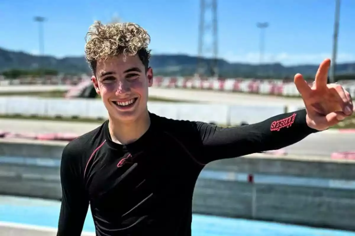 Joven sonriente con camiseta negra de manga larga levantando la mano y haciendo el signo de la paz en una pista de carreras al aire libre Joven sonriente con camiseta negra de manga larga levantando la mano y haciendo el signo de la paz en una pista de carreras al aire libre