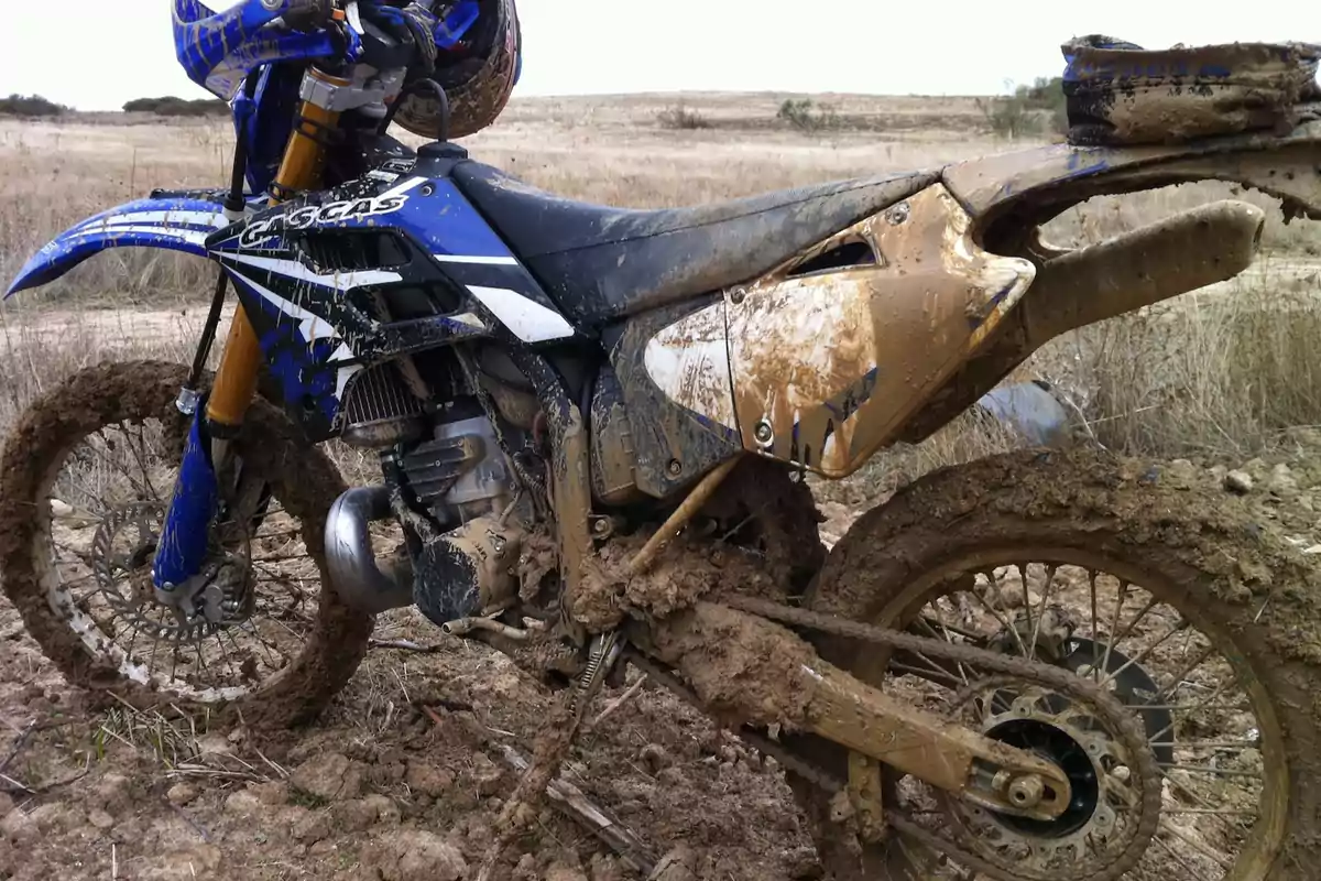 Motocicleta de enduro azul cubierta de lodo en un terreno seco y fangoso Motocicleta de enduro azul cubierta de lodo en un terreno seco y fangoso