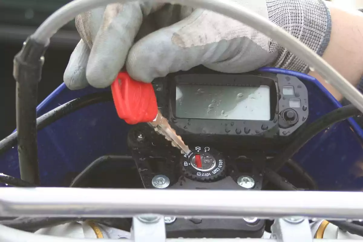Mano con guante girando la llave de encendido de una motocicleta mojada Mano con guante girando la llave de encendido de una motocicleta mojada