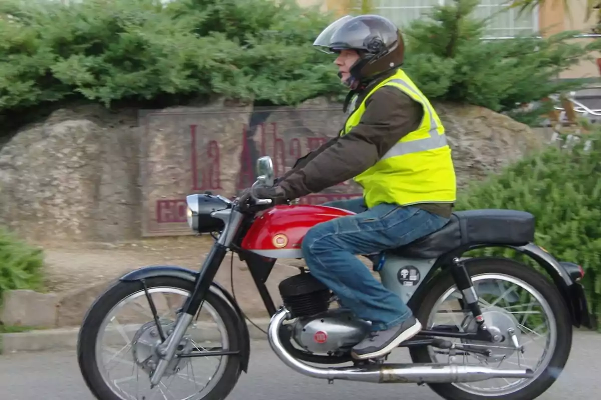 Hombre con casco y chaleco reflectante conduciendo una motocicleta clásica roja en la calle Hombre con casco y chaleco reflectante conduciendo una motocicleta clásica roja en la calle