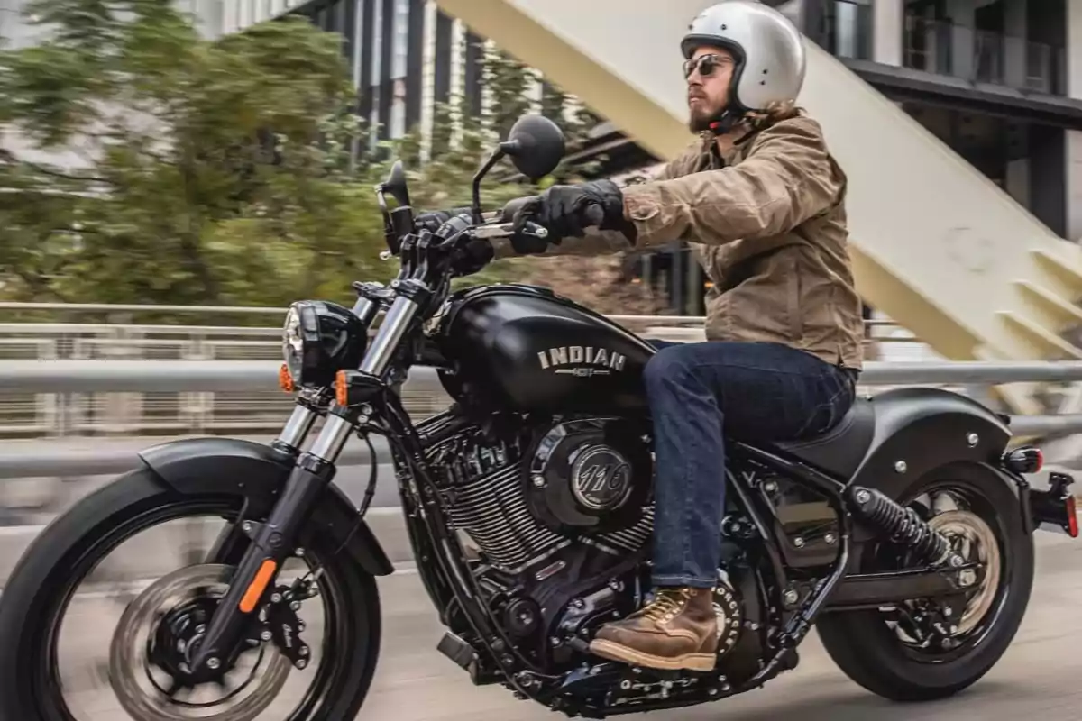 Man riding a black Indian motorcycle through the city wearing a helmet and sunglasses