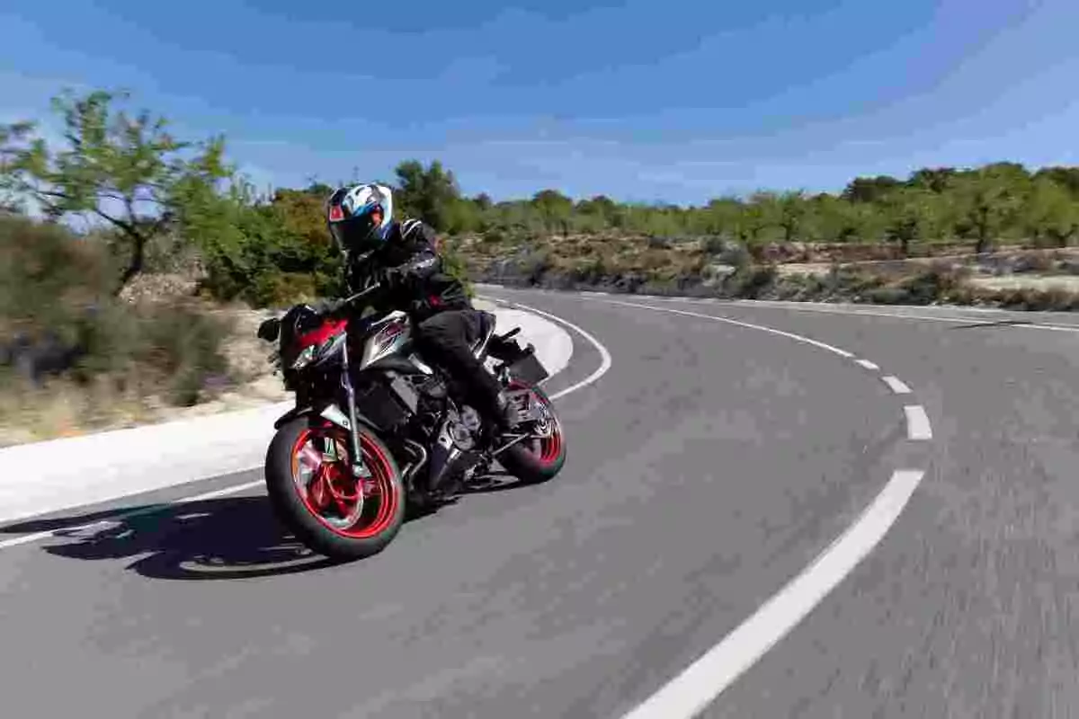 Person riding a sport motorcycle on a winding road surrounded by greenery under a clear sky Person riding a sport motorcycle on a winding road surrounded by greenery under a clear sky