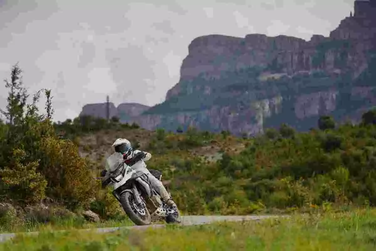 Person riding a motorcycle on a road surrounded by vegetation with mountains in the background Person riding a motorcycle on a road surrounded by vegetation with mountains in the background