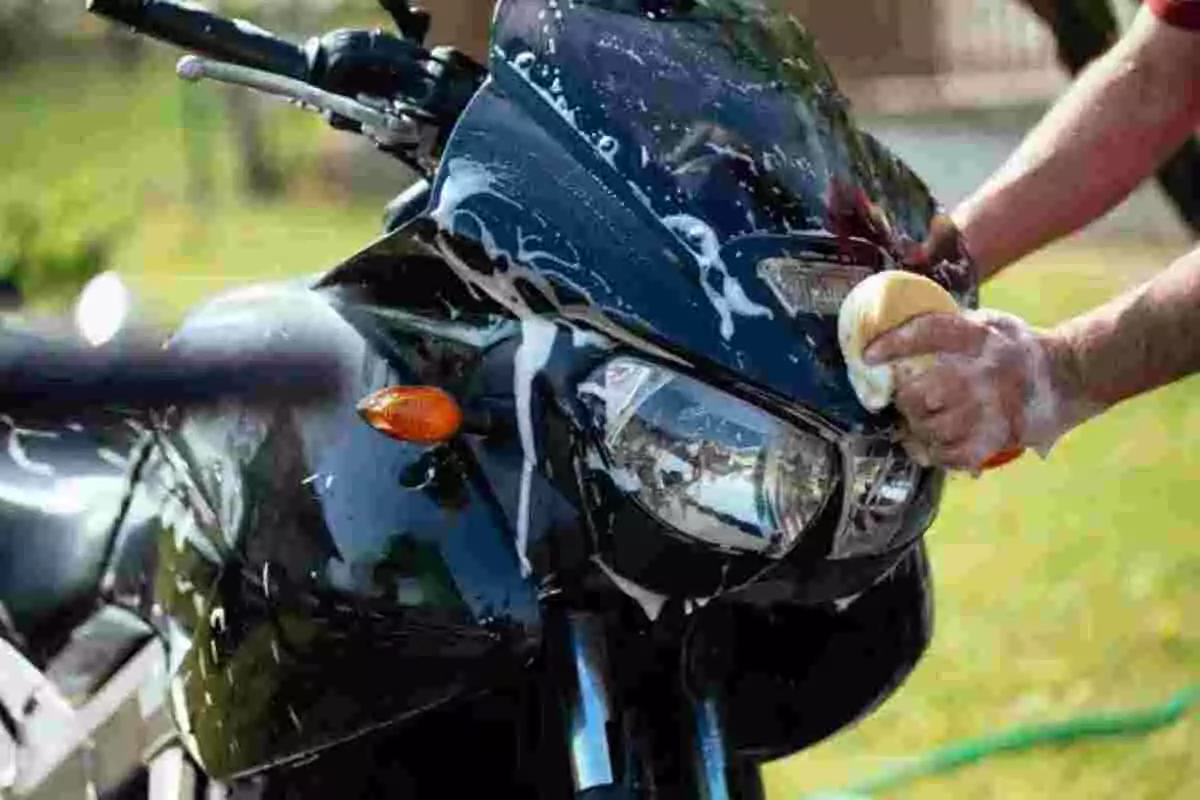 Persona lavando una motocicleta negra con una esponja y jabón Persona lavando una motocicleta negra con una esponja y jabón