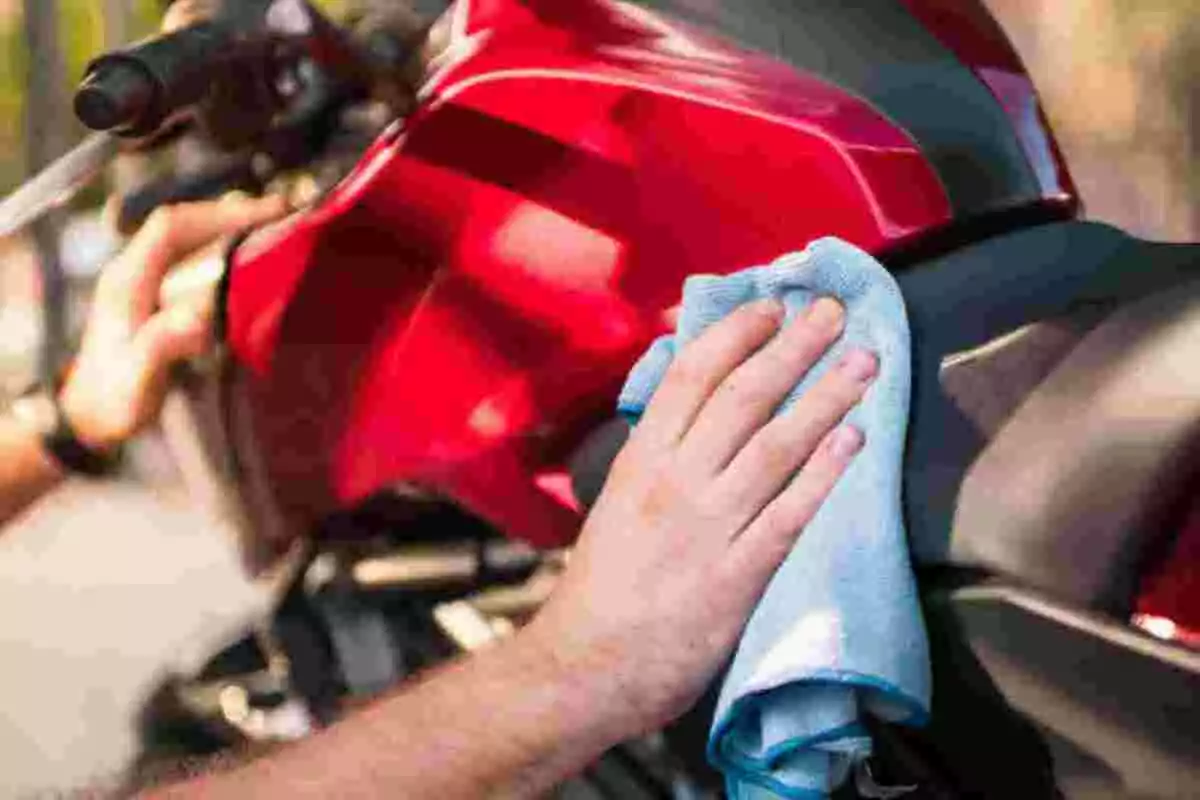 Persona limpiando el tanque de una motocicleta roja con un trapo azul Persona limpiando el tanque de una motocicleta roja con un trapo azul