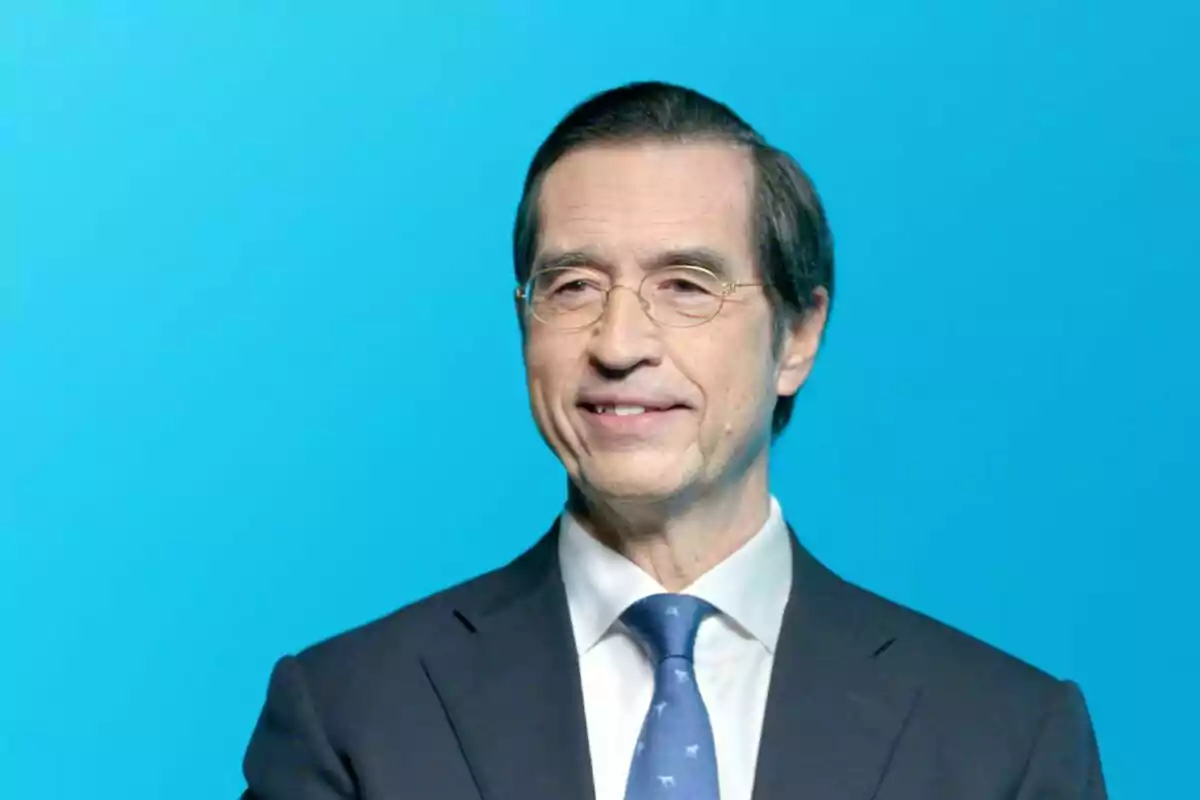 Hombre de mediana edad con gafas y traje oscuro sonriendo frente a un fondo azul Hombre de mediana edad con gafas y traje oscuro sonriendo frente a un fondo azul