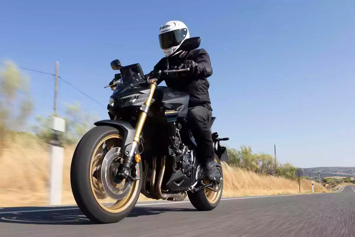 Persona conduciendo una motocicleta negra en una carretera bajo un cielo despejado