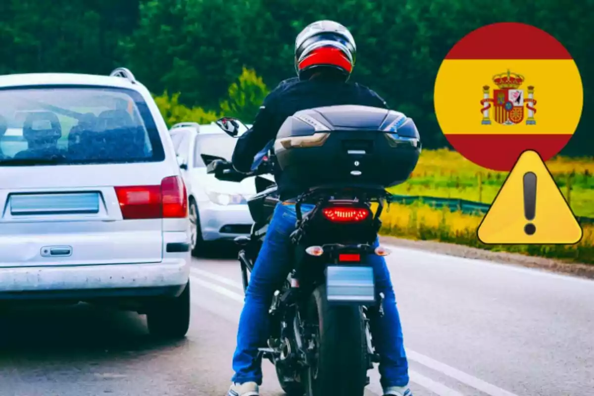 Motociclista con casco rojo y negro circulando entre autos en una carretera junto a un símbolo de advertencia y la bandera de España Motociclista con casco rojo y negro circulando entre autos en una carretera junto a un símbolo de advertencia y la bandera de España
