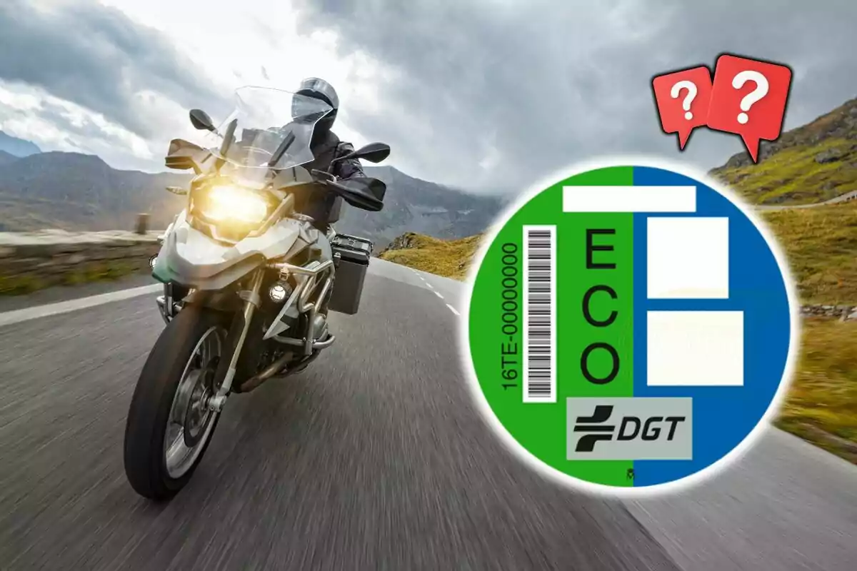 Motocicleta circulando por una carretera de montaña con una etiqueta ecológica de la DGT en primer plano y dos iconos de interrogación en la esquina superior derecha.