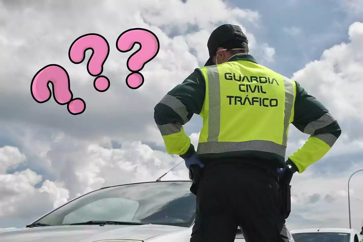 Agente de la Guardia Civil de Tráfico de espaldas junto a un coche con signos de interrogación rosas sobre un cielo nublado