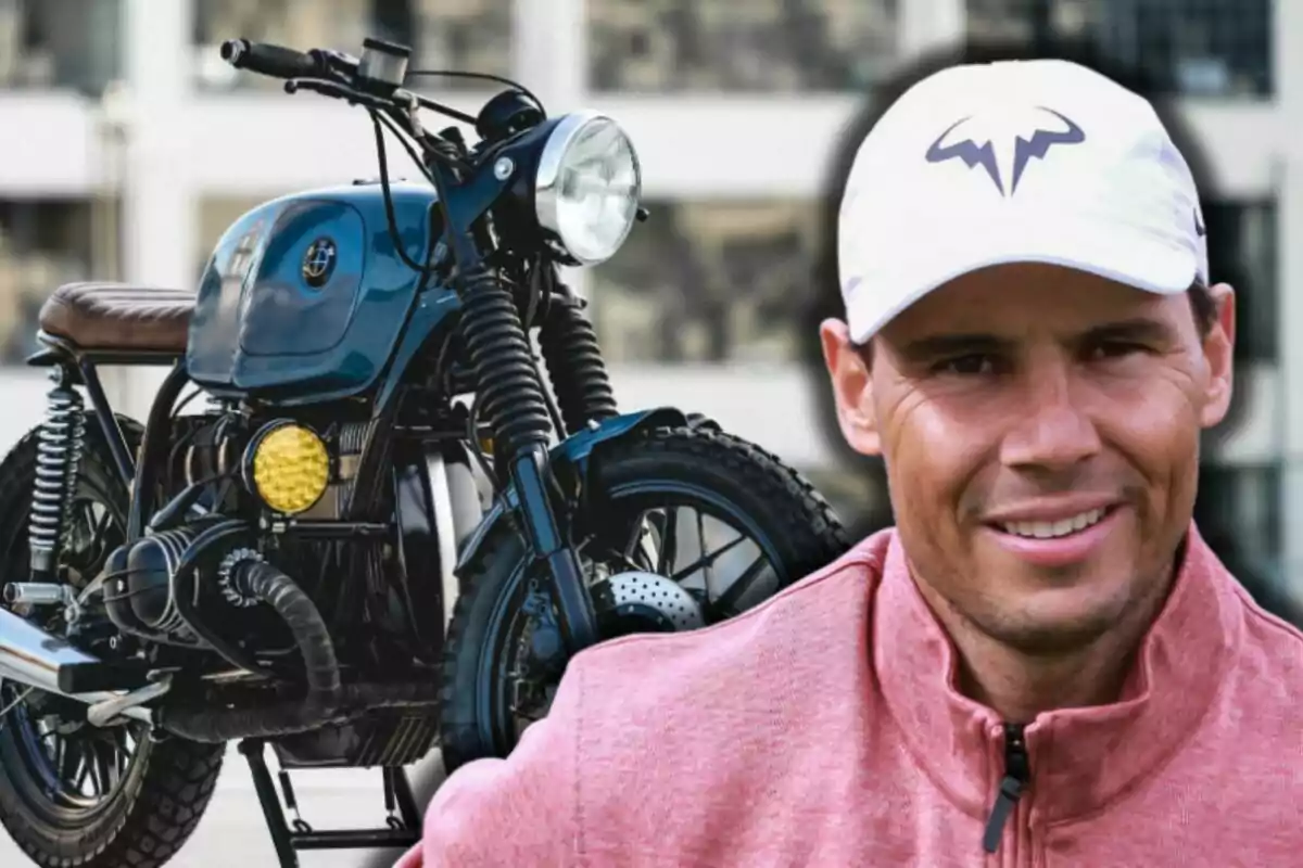 Rafa Nadal con gorra blanca y chaqueta rosa sonríe frente a una motocicleta clásica azul con asiento marrón
