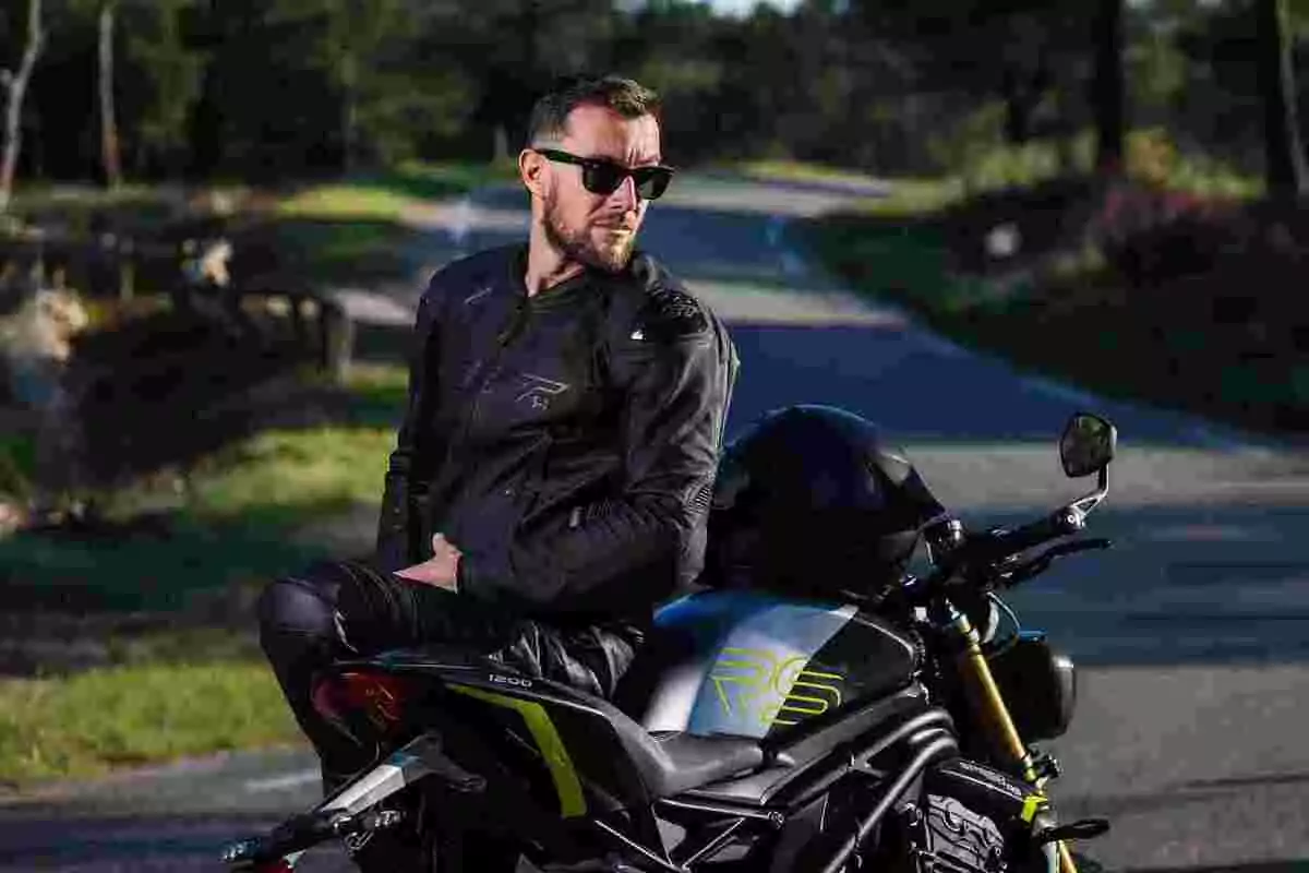 Man with a jacket and sunglasses sitting on a sport motorcycle on a road surrounded by nature