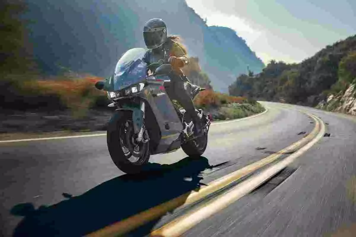 Persona conduciendo una motocicleta deportiva plateada en una carretera de montaña con curvas rodeada de naturaleza y montañas al fondo Persona conduciendo una motocicleta deportiva plateada en una carretera de montaña con curvas rodeada de naturaleza y montañas al fondo
