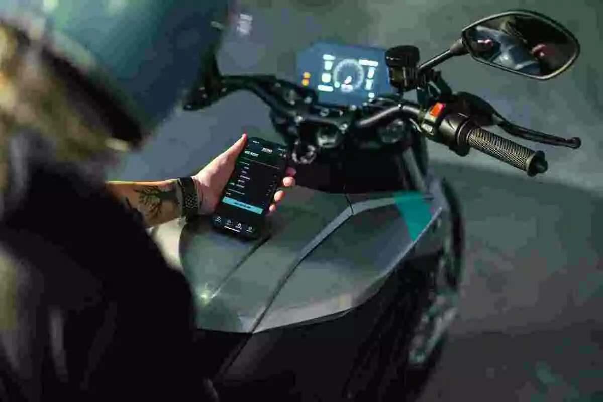 Persona con casco sostiene un teléfono móvil frente al tablero digital de una motocicleta Persona con casco sostiene un teléfono móvil frente al tablero digital de una motocicleta