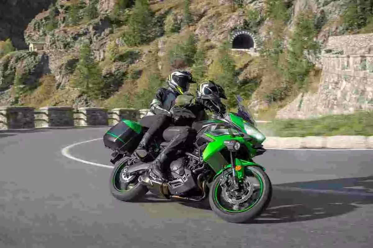 Dos personas con equipo de protección manejan una motocicleta verde en una carretera de montaña con curvas y paisaje rocoso de fondo Dos personas con equipo de protección manejan una motocicleta verde en una carretera de montaña con curvas y paisaje rocoso de fondo