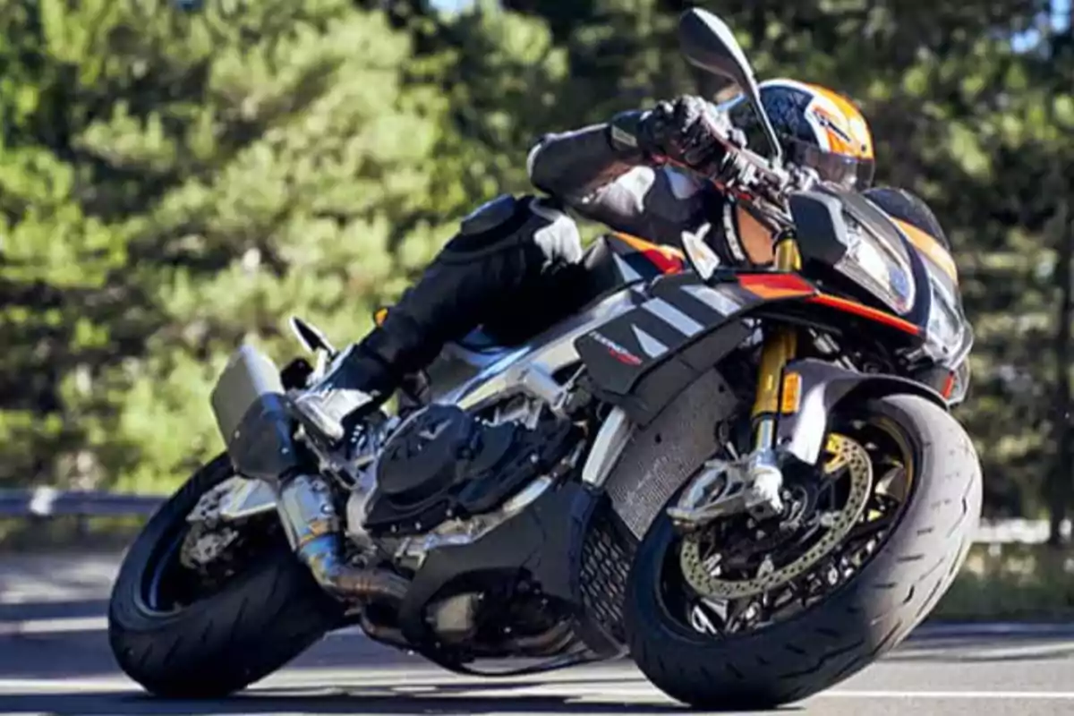 Motociclista tomando una curva en carretera rodeada de árboles