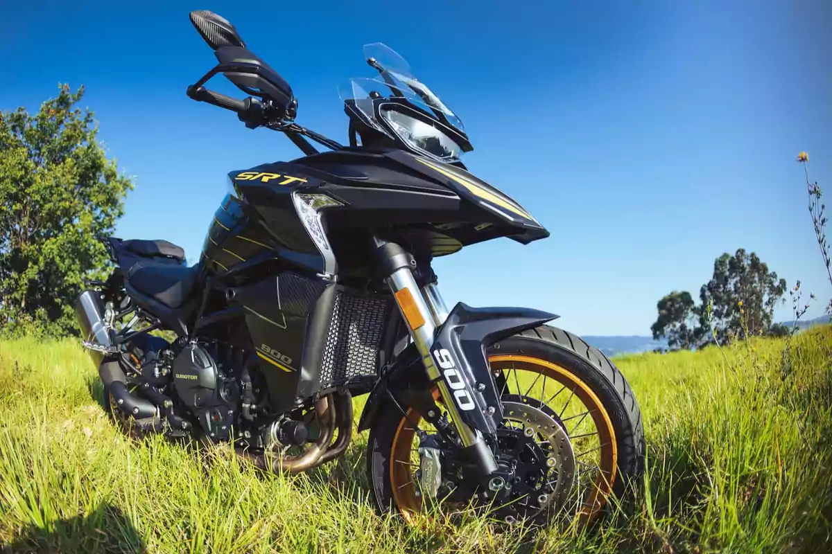 Motocicleta deportiva negra con detalles dorados estacionada sobre césped bajo un cielo azul despejado Motocicleta deportiva negra con detalles dorados estacionada sobre césped bajo un cielo azul despejado