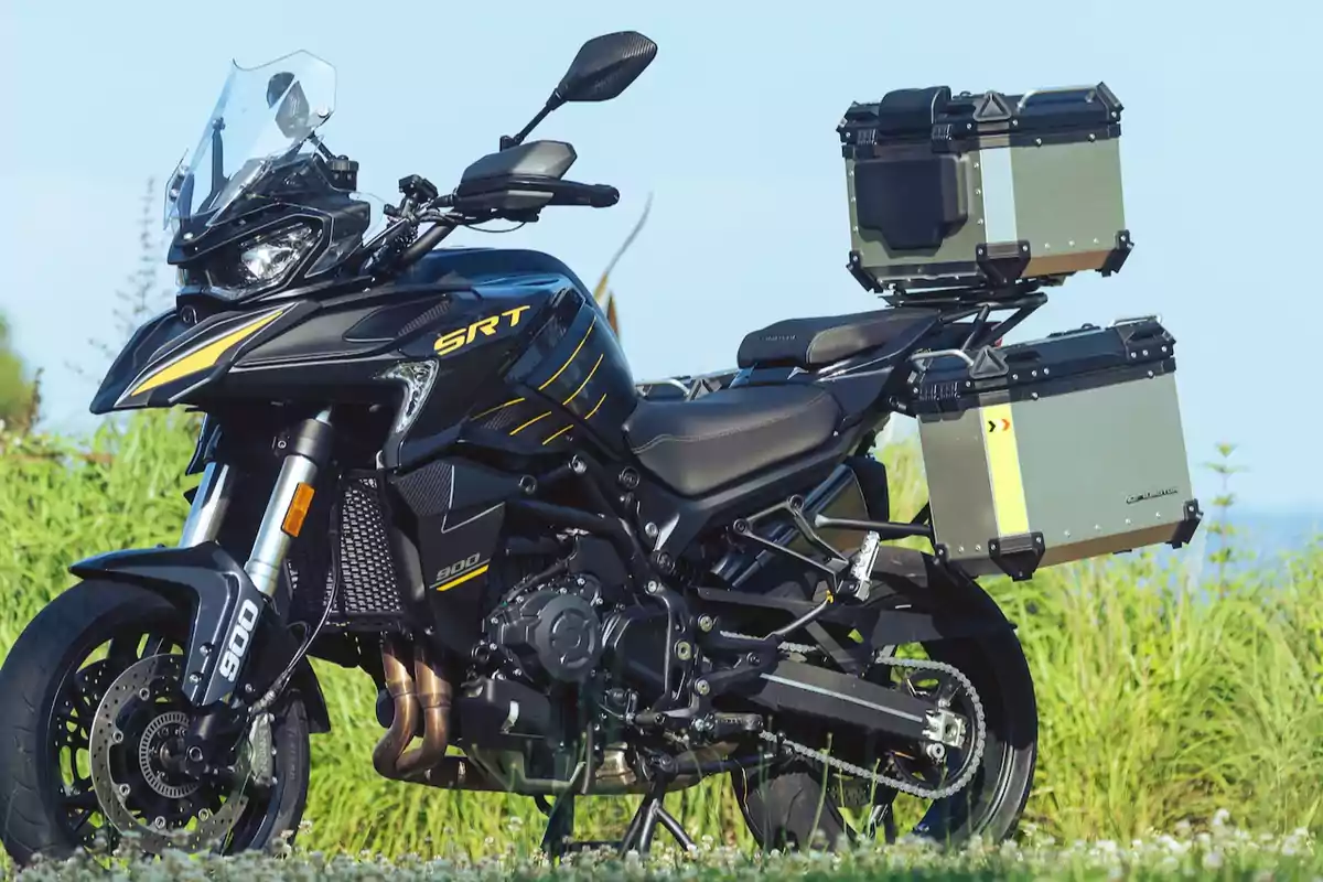 Motocicleta negra con detalles amarillos equipada con maletas de aluminio estacionada sobre césped con vegetación al fondo Motocicleta negra con detalles amarillos equipada con maletas de aluminio estacionada sobre césped con vegetación al fondo