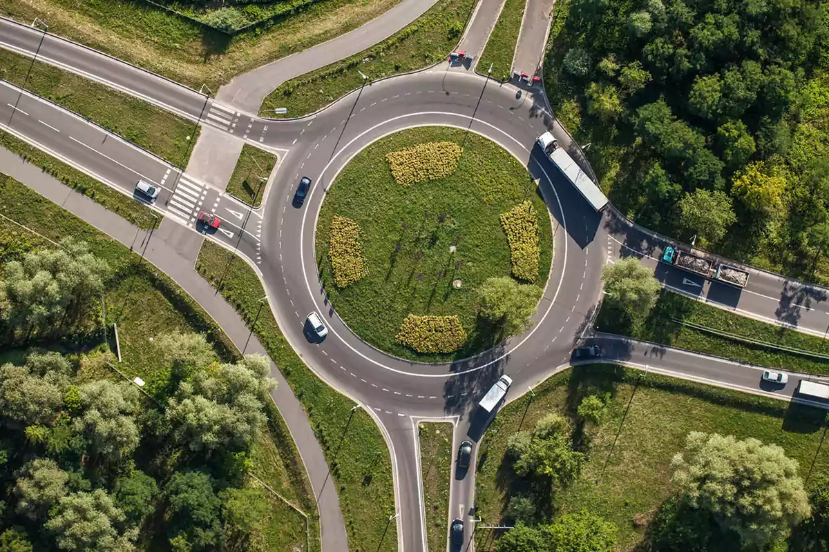 Vista aérea de una glorieta rodeada de vegetación con varios coches y camiones circulando por las diferentes entradas y salidas del cruce Vista aérea de una glorieta rodeada de vegetación con varios coches y camiones circulando por las diferentes entradas y salidas del cruce