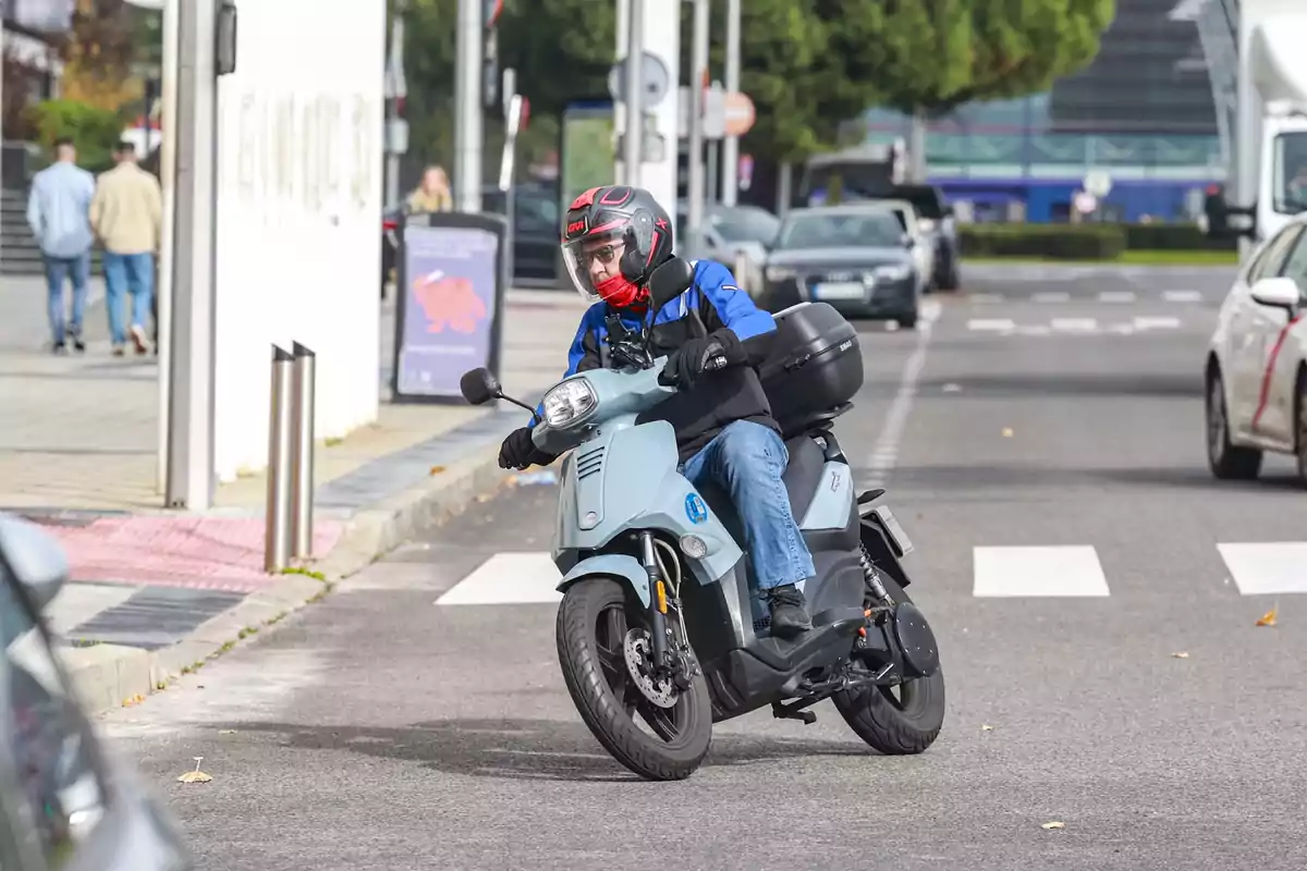 Persona conduciendo una moto azul claro en una calle urbana con tráfico y paso de peatones Persona conduciendo una moto azul claro en una calle urbana con tráfico y paso de peatones