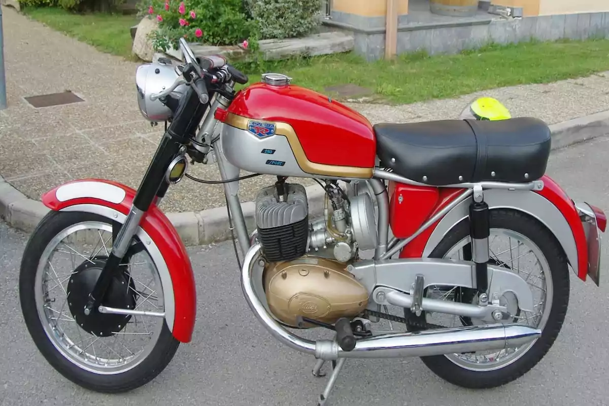 Motocicleta clásica de color rojo y plateado estacionada en la calle junto a una acera y un jardín. Motocicleta clásica de color rojo y plateado estacionada en la calle junto a una acera y un jardín.