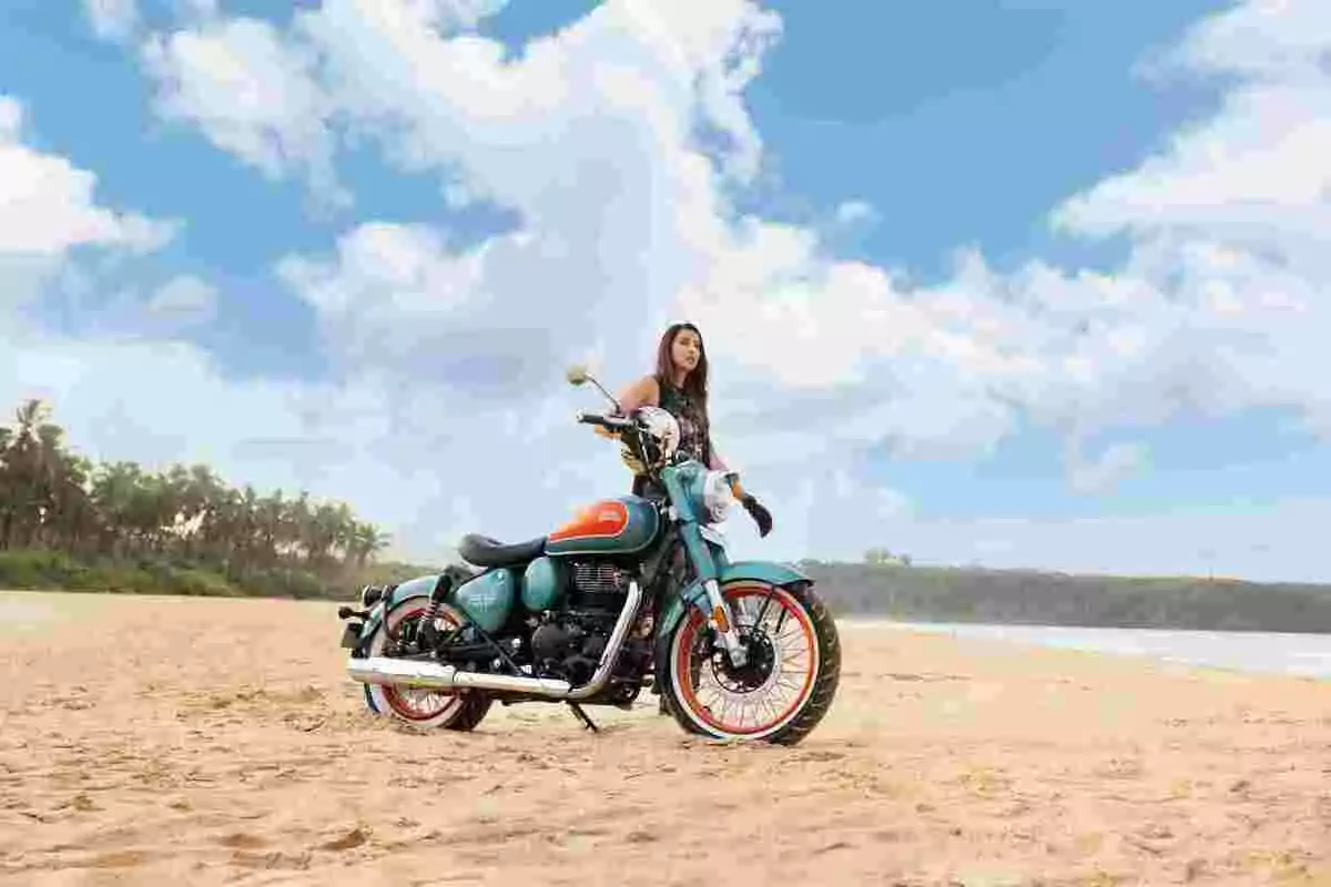 Dona posant al costat d’una motocicleta a la platja amb cel blau i núvols al fons Dona posant al costat d’una motocicleta a la platja amb cel blau i núvols al fons