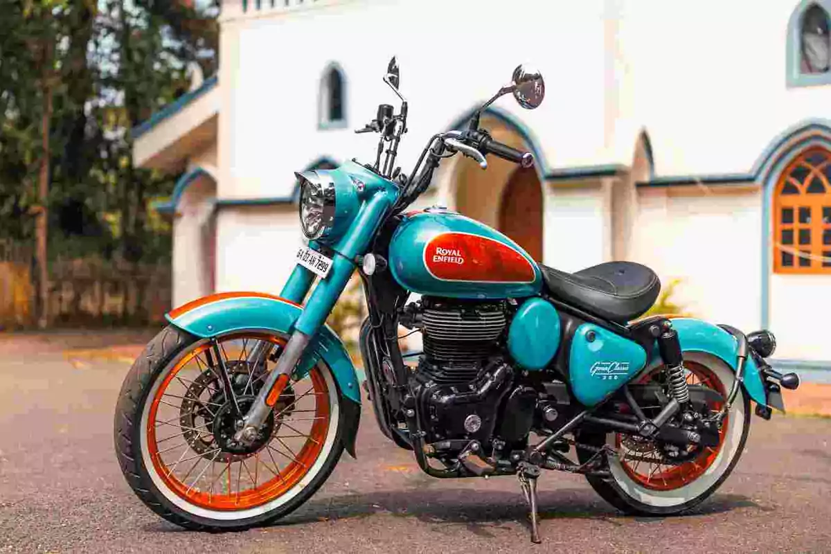 Motocicleta Royal Enfield blava amb detalls taronges estacionada davant d’un edifici blanc Motocicleta Royal Enfield blava amb detalls taronges estacionada davant d’un edifici blanc