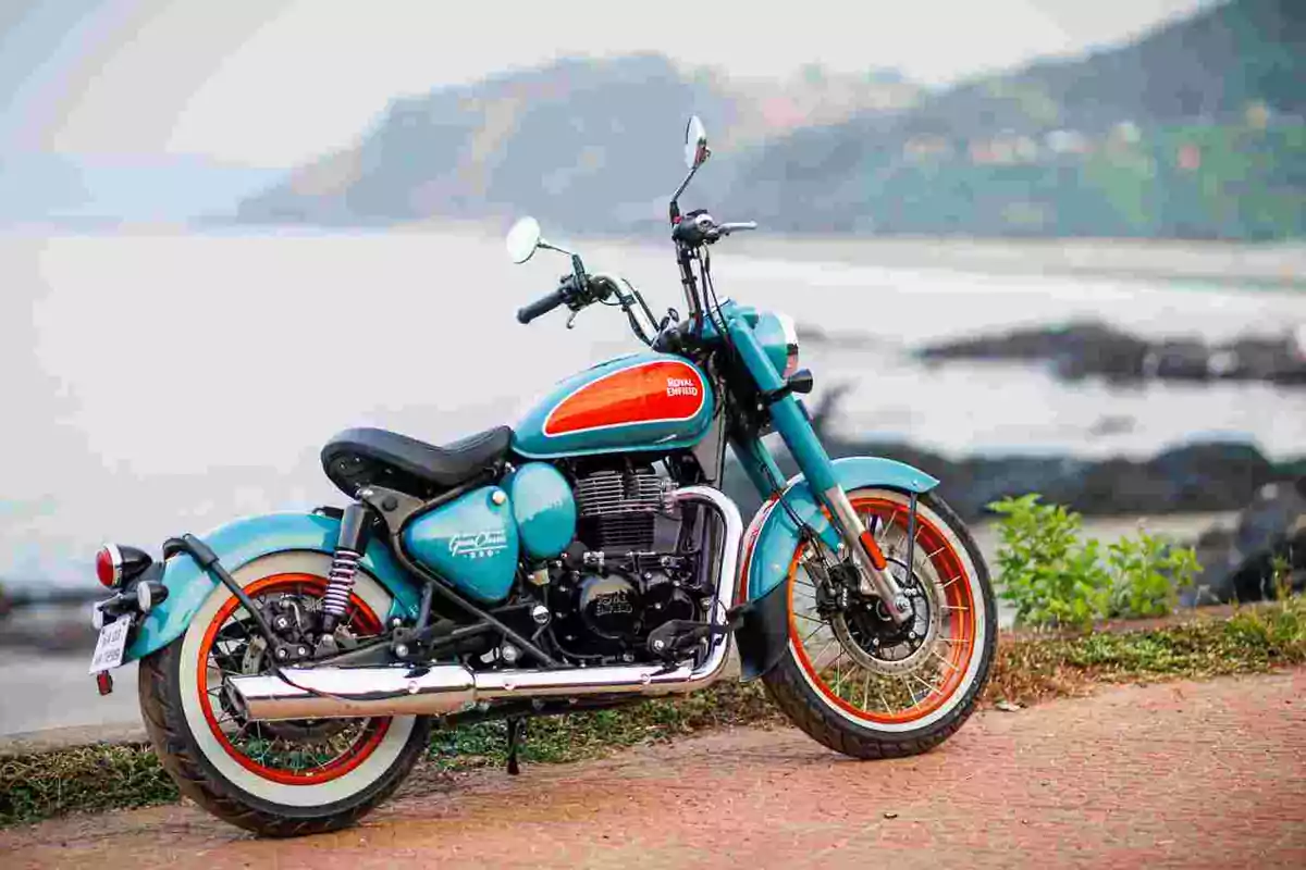 Motocicleta blava amb detalls taronja estacionada al costat d’un camí amb vista al mar i muntanyes al fons Motocicleta blava amb detalls taronja estacionada al costat d’un camí amb vista al mar i muntanyes al fons