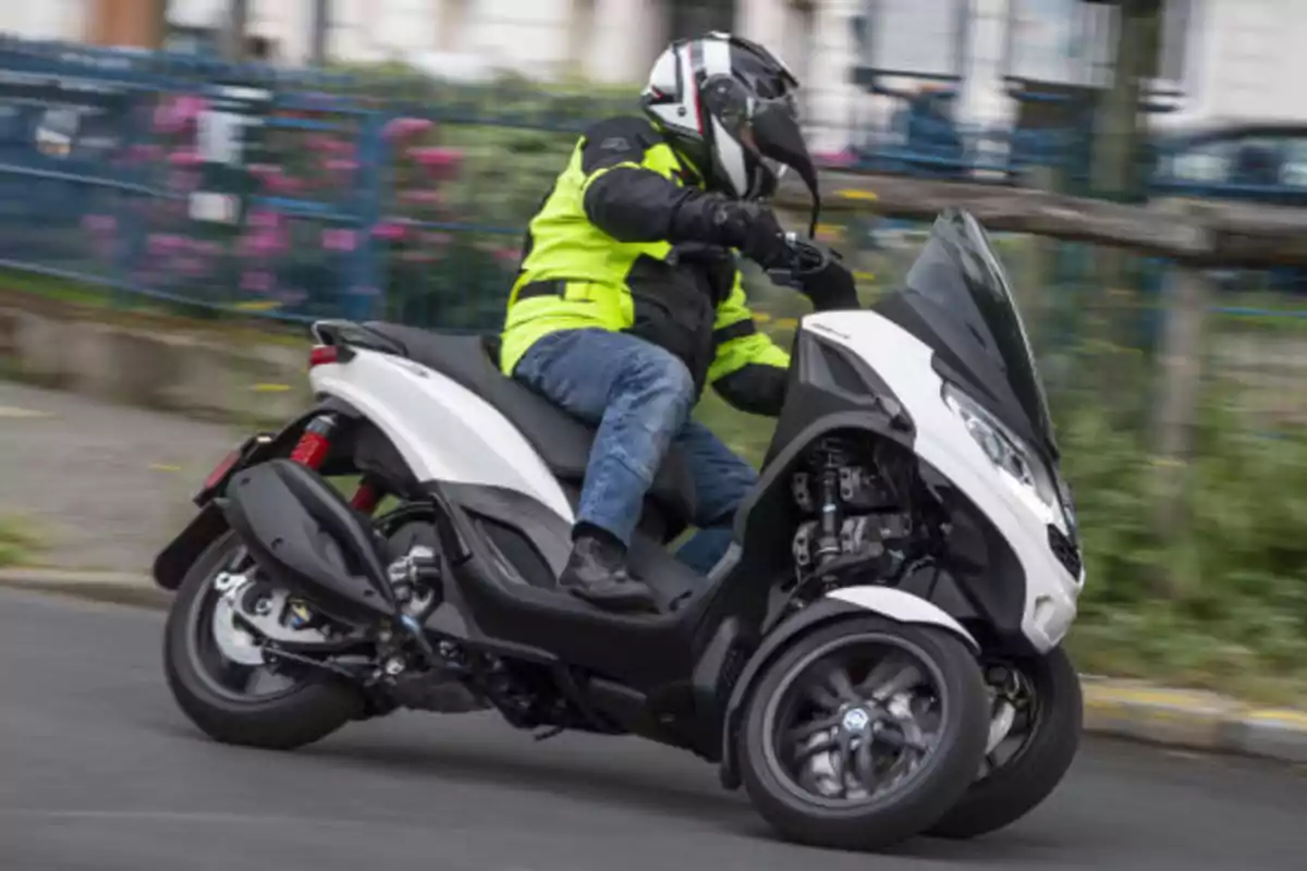 Persona conduciendo una moto de tres ruedas con chaqueta amarilla y casco en una calle urbana
