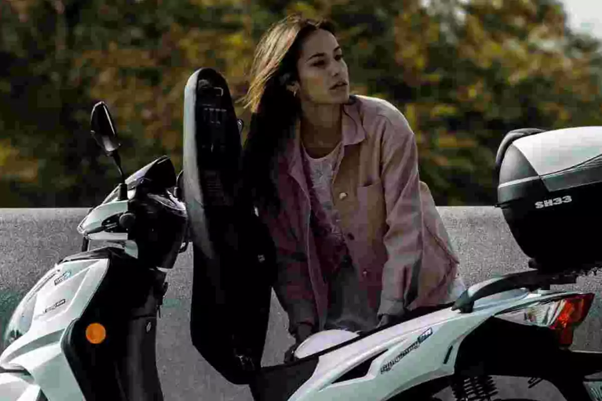 Mujer con chaqueta rosa guardando un casco en el compartimento de una moto blanca Mujer con chaqueta rosa guardando un casco en el compartimento de una moto blanca