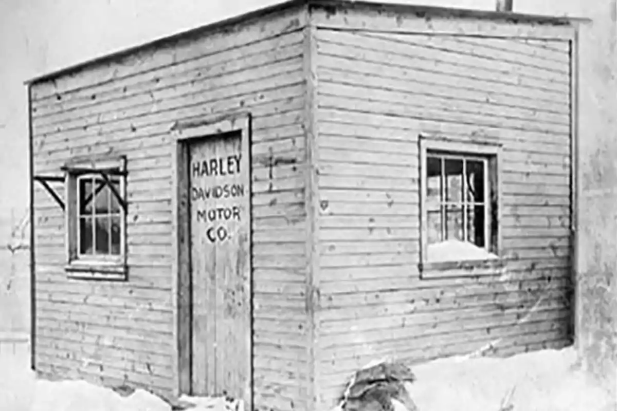Pequeña cabaña de madera con dos ventanas y una puerta que tiene escrito Harley Davidson Motor Co en un entorno nevado Pequeña cabaña de madera con dos ventanas y una puerta que tiene escrito Harley Davidson Motor Co en un entorno nevado