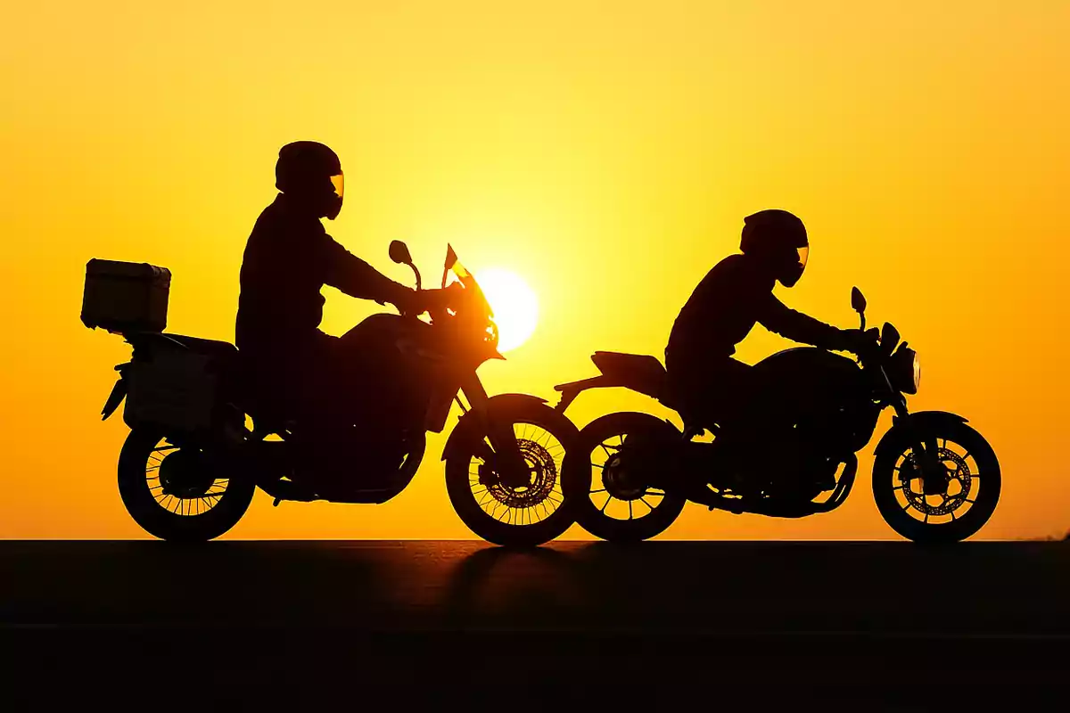 Dos personas en motocicleta conduciendo al atardecer con el sol de fondo Dos personas en motocicleta conduciendo al atardecer con el sol de fondo