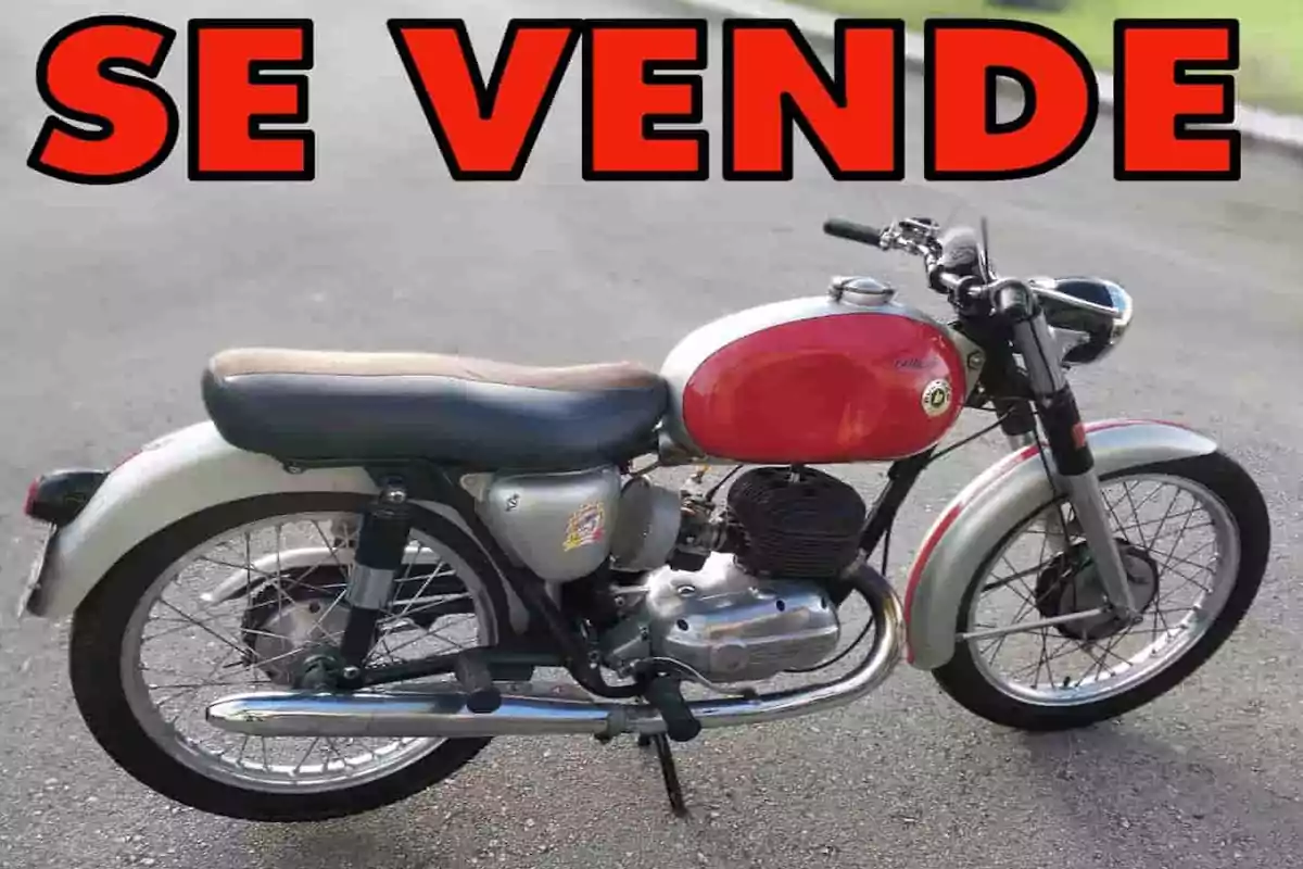 Motocicleta clásica estacionada en la calle con un letrero grande en letras rojas que dice SE VENDE
