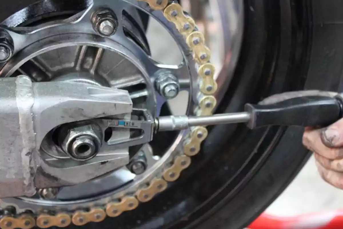 Persona ajustant la cadena d’una motocicleta amb una eina manual Persona ajustant la cadena d’una motocicleta amb una eina manual