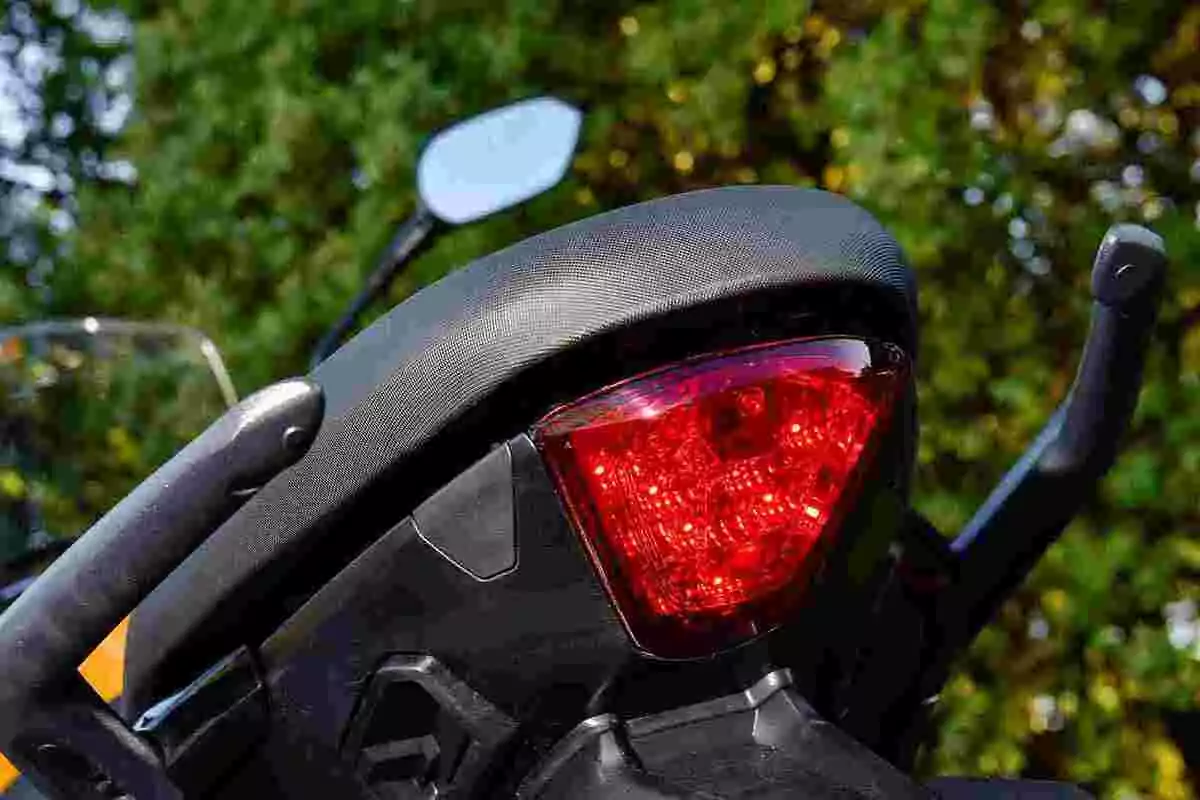 Luz trasera de una motocicleta encendida con fondo de árboles verdes Luz trasera de una motocicleta encendida con fondo de árboles verdes