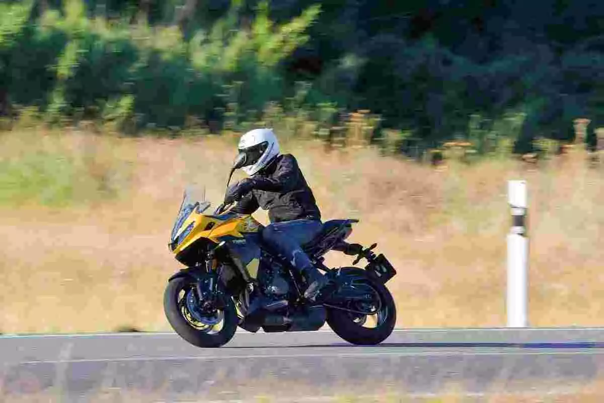 Persona conduciendo una motocicleta amarilla en una carretera con vegetación al fondo Persona conduciendo una motocicleta amarilla en una carretera con vegetación al fondo