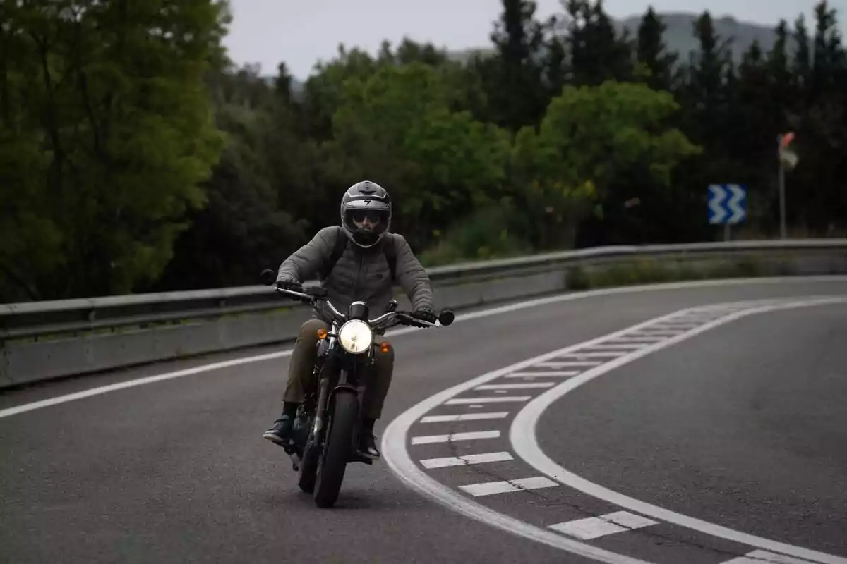 Persona conduciendo una motocicleta en una carretera curva rodeada de árboles y vegetación. Persona conduciendo una motocicleta en una carretera curva rodeada de árboles y vegetación.