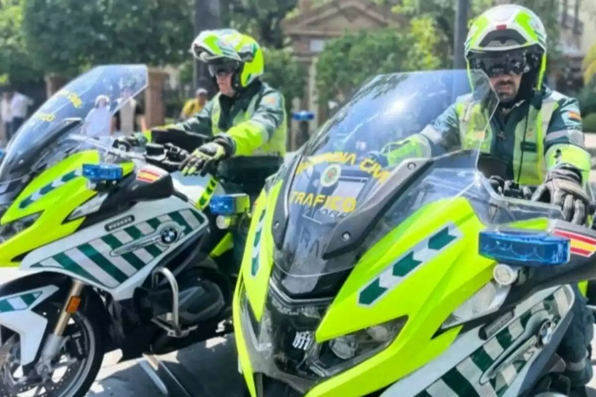 Dos agents de trànsit amb uniforme i casc condueixen motocicletes BMW de la Guàrdia Civil en un carrer urbà. Dos agents de trànsit amb uniforme i casc condueixen motocicletes BMW de la Guàrdia Civil en un carrer urbà.
