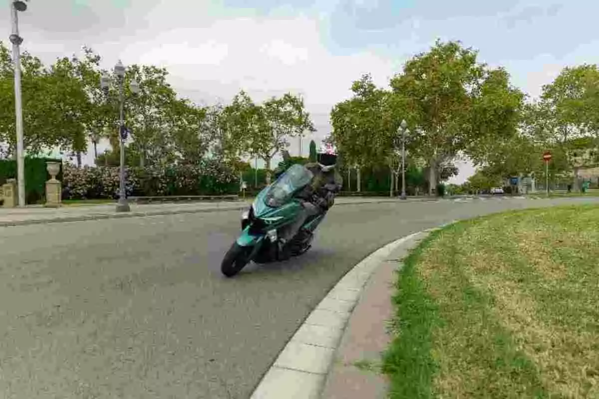 Persona conduciendo una motocicleta verde en una curva de una calle rodeada de árboles y césped Persona conduciendo una motocicleta verde en una curva de una calle rodeada de árboles y césped