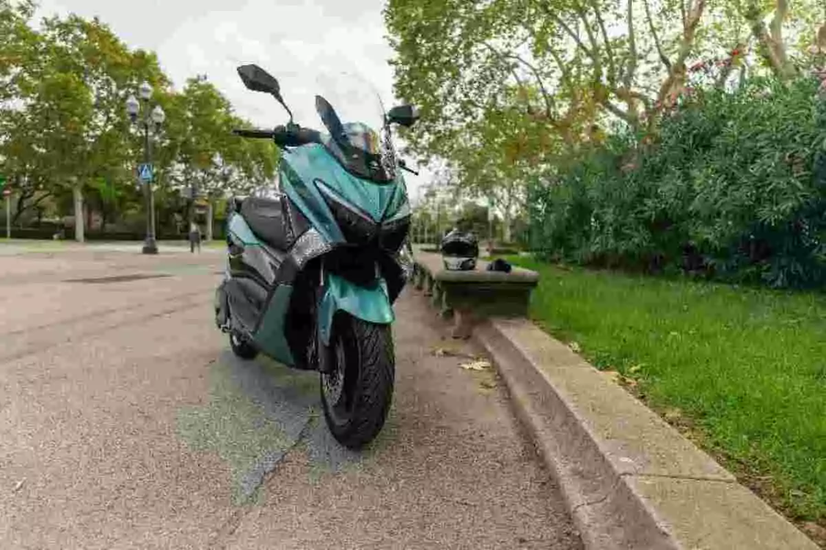 Motocicleta azul estacionada junto a una banqueta en un parque con árboles y un casco sobre una banca Motocicleta azul estacionada junto a una banqueta en un parque con árboles y un casco sobre una banca