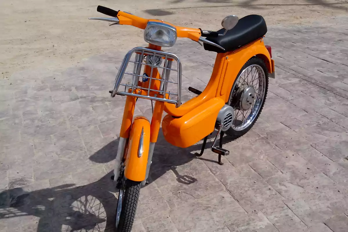 Motocicleta antigua de color naranja estacionada sobre un suelo de adoquines Motocicleta antigua de color naranja estacionada sobre un suelo de adoquines