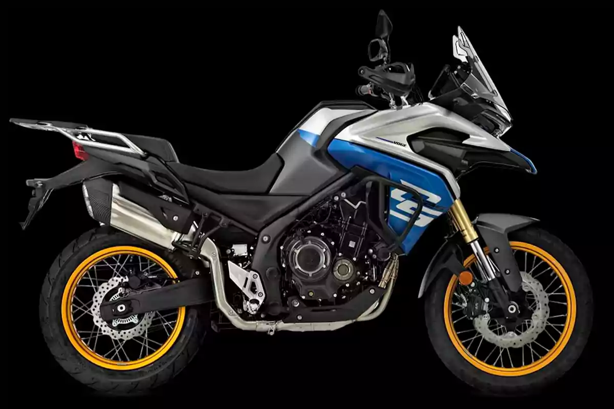 Motocicleta tipo adventure de color negro, azul y plateado con rines dorados sobre fondo negro Motocicleta tipo adventure de color negro, azul y plateado con rines dorados sobre fondo negro