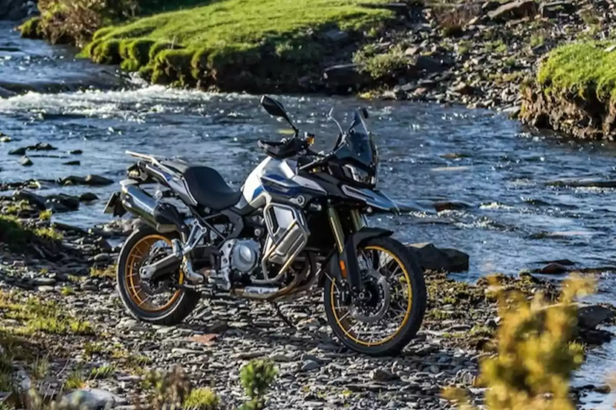 Motocicleta de aventura estacionada junto a un río rodeado de vegetación y piedras Motocicleta de aventura estacionada junto a un río rodeado de vegetación y piedras