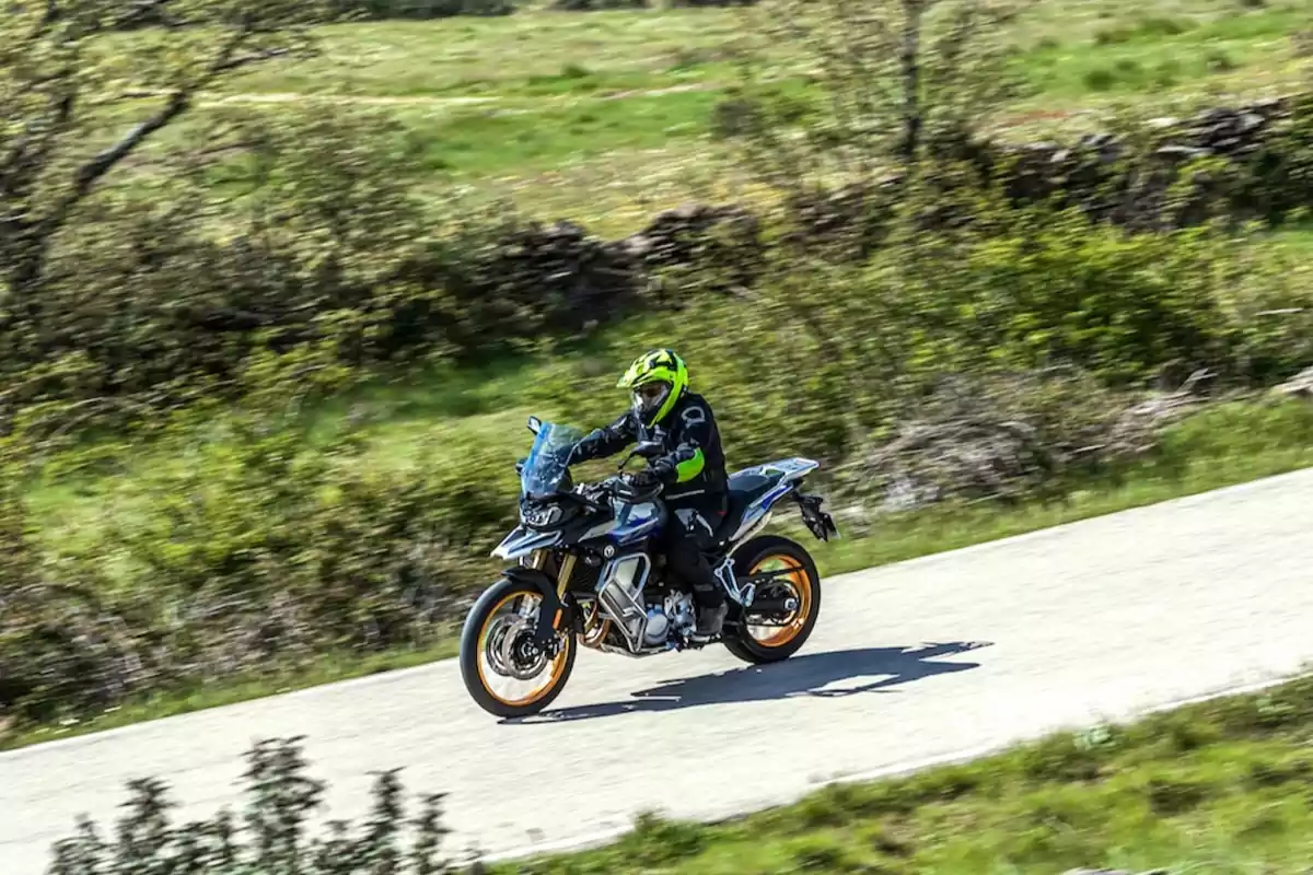 Persona conduciendo una motocicleta deportiva en una carretera rodeada de vegetación Persona conduciendo una motocicleta deportiva en una carretera rodeada de vegetación