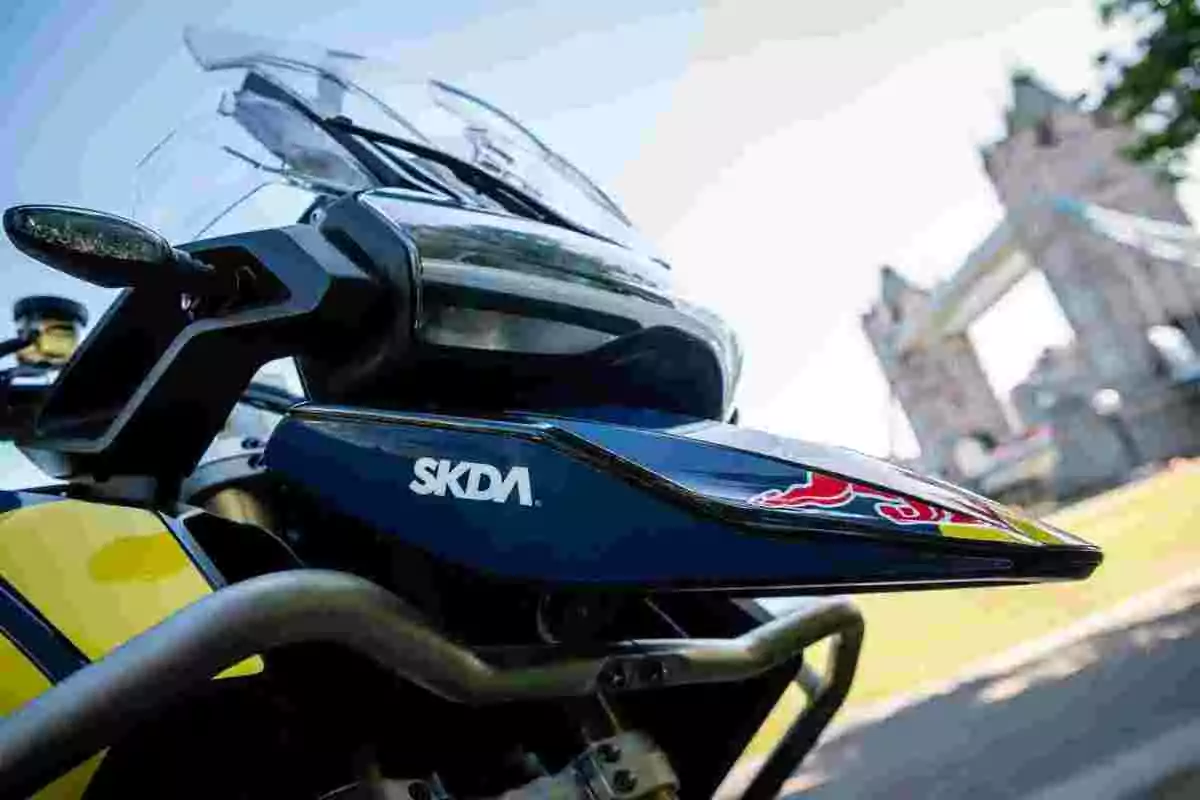 Motocicleta amarilla y azul con protector de mano SKDA y el puente Tower Bridge desenfocado al fondo Motocicleta amarilla y azul con protector de mano SKDA y el puente Tower Bridge desenfocado al fondo